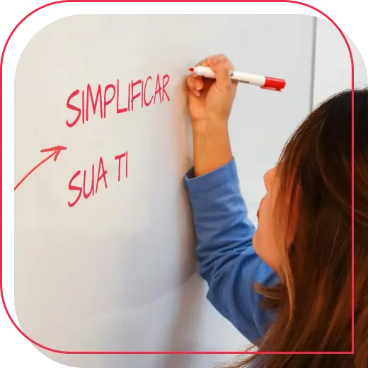 Mulher escrevendo em um quadro branco com marcador vermelho. As palavras ‘Simplificar sua TI’ estão escritas.